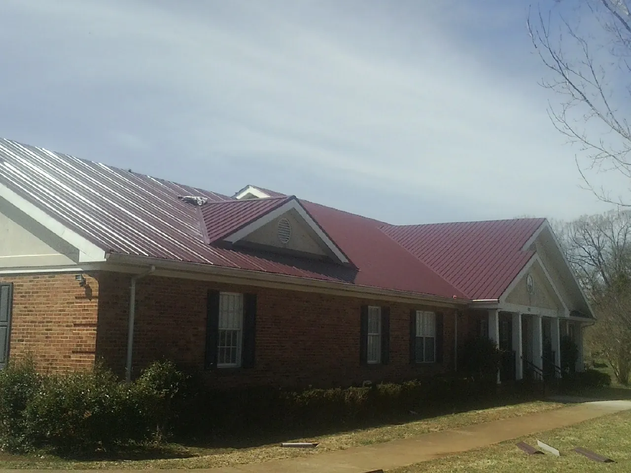 Red metal roof with gabled entries on a long brick building, from a Hail Damage Roof Repair job in East Peoria