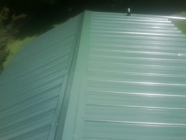 New green metal panels meeting at the ridge of a roof — Flat Roof Repair work by our crew in East Peoria