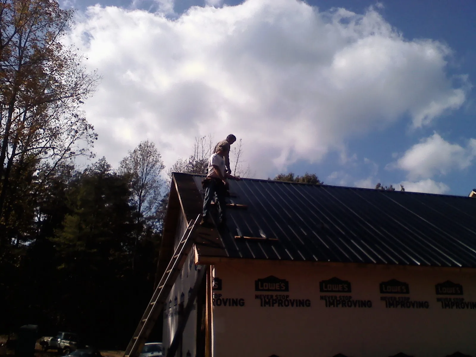 Roofer fastening dark metal panels high against a cloudy sky, from a Roof Inspection job in East Peoria