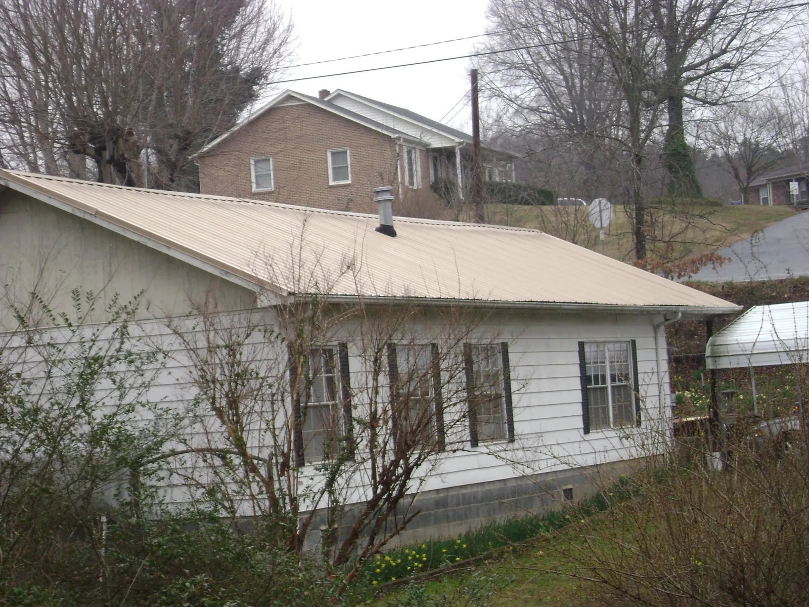 Tan metal roof on a white sided house set into a hillside — Commercial Roofing by Roofing Brothers in East Peoria