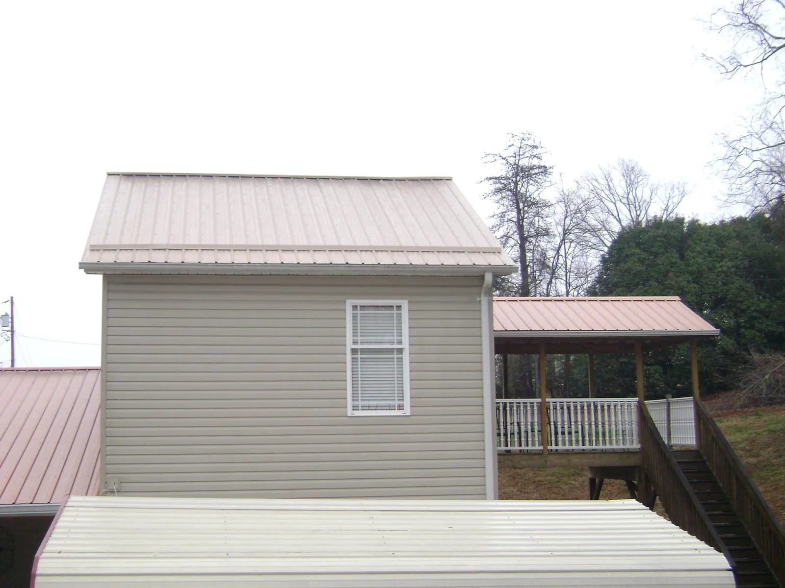 Tan metal roofs on a two story addition and attached porch, from a Roof Replacement job in East Peoria